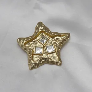 Close up of vintage molten star brooch featuring textured gold finish and three square crystals.