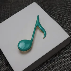 Close-up detail of the turquoise enamel music note brooch, showing fine gold metal trim.