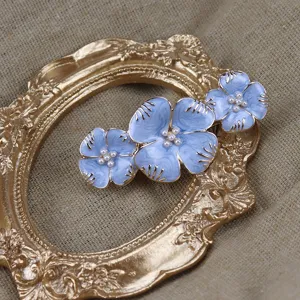 Détail de pince à cheveux fleur émail bleu vintage, centre perlé et bordure dorée.