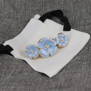 Gros plan détaillé d'une pince à cheveux fleur en émail bleu avec perles, accessoire élégant.
