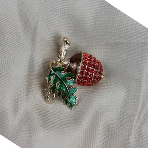 Primo piano dettaglio spilla vintage ghianda strass rossi e foglia quercia smaltata verde.