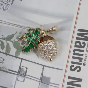 Primo piano di spilla vintage a ghianda in strass con foglia di quercia smaltata verde su giornale.
