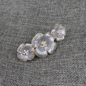 Gros plan de pince a cheveux fleur de perle emaillee retro, texture marbre gris, elegant.