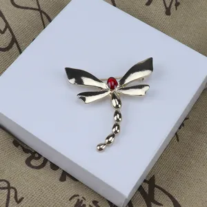 Detail view of a vintage enameled alloy dragonfly brooch with red stone, elegant clothing accessory.
