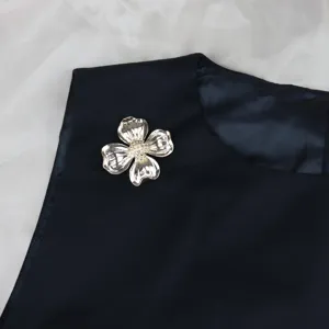 Close-up of vintage metal four-leaf clover flower brooch with sparkling rhinestone center.