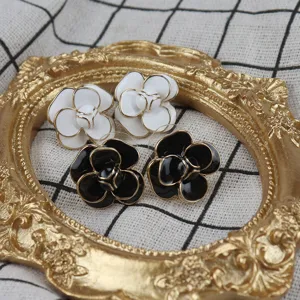 Close-up of black and white camellia enamel stud earrings with gold-tone metal trim.