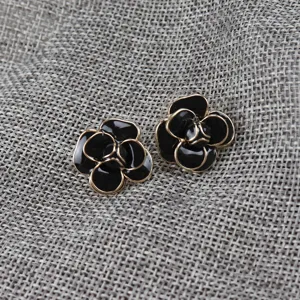 Close-up detail of black camellia floral enamel drop glaze stud earrings with golden edge.