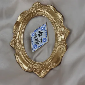 Exquisite rhombus enamel brooch with delicate floral pattern, displayed in a vintage frame.