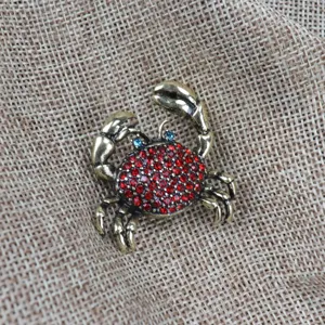 Nahaufnahme einer vintage bronzefarbenen Krebs-Brosche mit roten und blauen Strasssteinen.