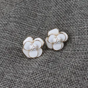 Camellia flower earrings close-up, white enamel petals with gold trim, detailed product shot view.
