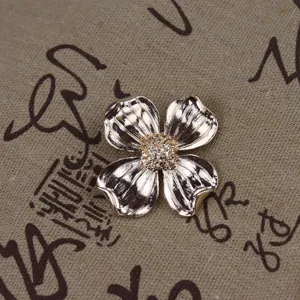 Vintage gold-tone metal four-petal flower brooch with textured finish and delicate stamen center.