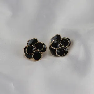 Detail view of the black camellia flower enamel earrings with metallic edges.