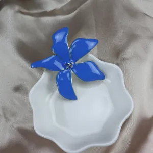 Close-up of a stunning blue enamel iris flower brooch resting in a white dish, exquisite detail.