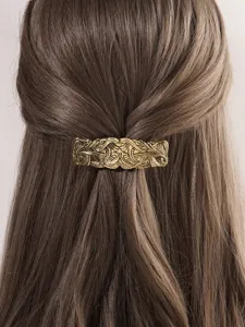 Detail shot of vintage gold alloy hair barrette with intricate engraved pattern worn on hair.