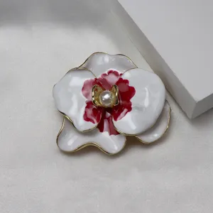 Detail shot of exquisite enamel orchid flower brooch with pearl center and gold edge on satin.