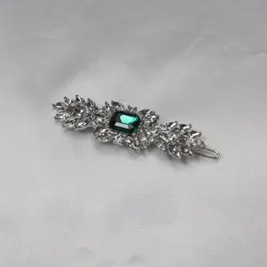 Detailed view of vintage crystal hair clip, featuring green stone and sparkling rhinestones.