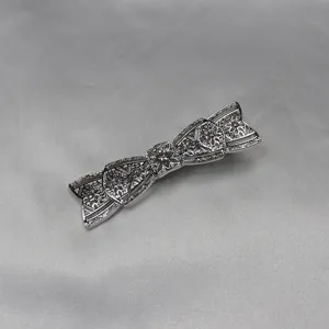 Silver vintage bow hairpin with intricate filigree hollow design and central rhinestone.