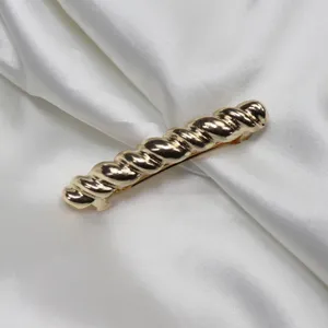 Closeup of a gold twisted metal hair clip on white satin, elegant accessory detail.