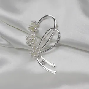 Close-up detail of silver-toned pearl and rhinestone brooch on white satin fabric.