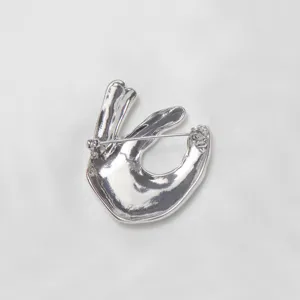 Silver metal OK hand gesture brooch detail view, stylish minimalist clothing accessory.