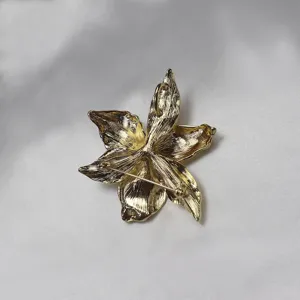 Gold metallic iris flower brooch pendant detail, textured floral jewelry close up view.