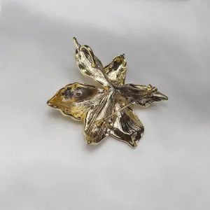 Detail view of gold-tone metal iris flower brooch pendant, showing back pin and loop structure.