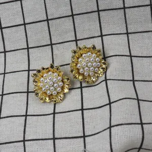 Gros plan détaillé de boucles d'oreilles puces fleurs dorées et perles avec design délicat.