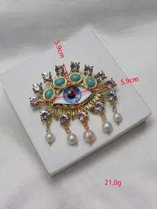 Exquisite evil eye brooch detail, gold-tone metal, sparkling rhinestones, and pearl drop.