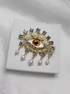 Exquisite surrealist evil eye brooch detailed with rhinestones and hanging pearls.