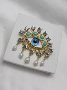 Evil eye brooch detail, gold-tone alloy with blue eye, rhinestones and dangling pearls.