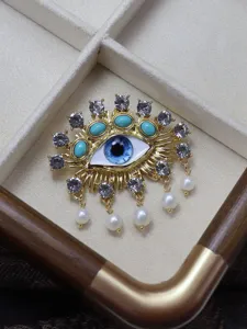 Evil eye brooch detailed closeup with sparkling rhinestones, turquoise stones, and dangling pearls.