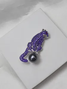 Detailed view of a silver-tone panther brooch encrusted with blue rhinestones and a dark pearl.