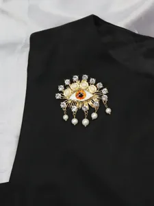 Gold-tone metal evil eye brooch with dazzling rhinestones, pearls and delicate hanging charms.