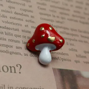 Primo piano di spilla a forma di fungo rosso e bianco vintage con pois cuore dorati.