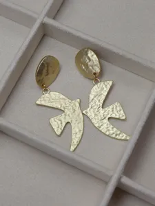 Detailed close-up shot of gold hammered dove earrings resting on a beige velvet tray.