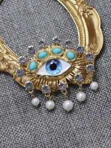 Close-up detail of luxury evil eye brooch with turquoise, crystals, and pearl drops.