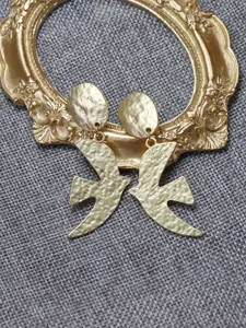 Detail shot of vintage gold dove earrings with textured finish on gray fabric background.