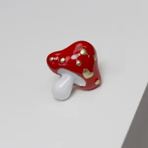 Primo piano dettaglio di una spilla a forma di fungo vintage smaltata rossa con pois oro.