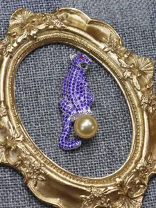 Detailed view of a stunning purple rhinestone leopard brooch holding a golden pearl accessory.