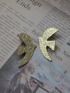 Close-up detail of vintage gold-toned dove bird stud earrings on retro newspaper background.