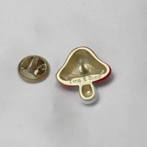 Dettaglio del retro della spilla a fungo carina e della chiusura in metallo su tessuto bianco.