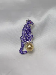 Detailed close-up view of a blue rhinestone leopard brooch featuring a golden pearl.