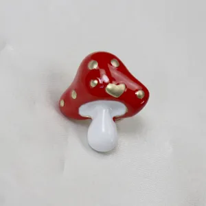 Dettaglio in primo piano della graziosa spilla a fungo smaltata rossa con pois dorati.