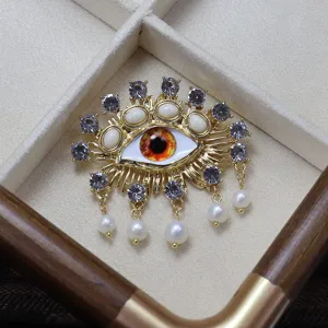 Exquisite devil eye brooch featuring sparkling crystals and pearls in gold tone finish.