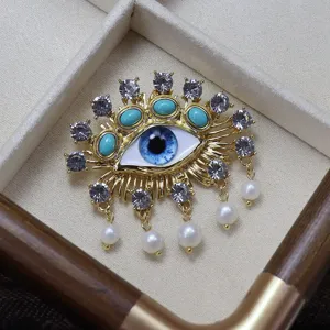 Exquisite evil eye brooch featuring sparkling rhinestones, turquoise stones and pearl dangles.