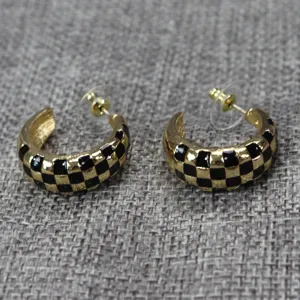 Vue détaillée de boucles d'oreilles créoles C émaillées à carreaux noir et or sur tissu.
