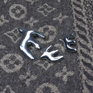 Close-up detail of silver swallow brooch and earrings set, polished metallic finish texture.