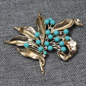 Vintage style gold-tone metal leaf and turquoise bead rhinestone brooch detail shot.
