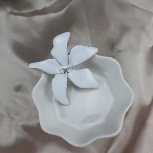White enamel iris flower brooch detail shot, elegant clothing accessory close-up display.