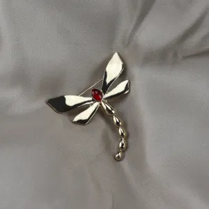 Vintage gold-plated dragonfly brooch featuring a red center stone, elegant clothing detail.